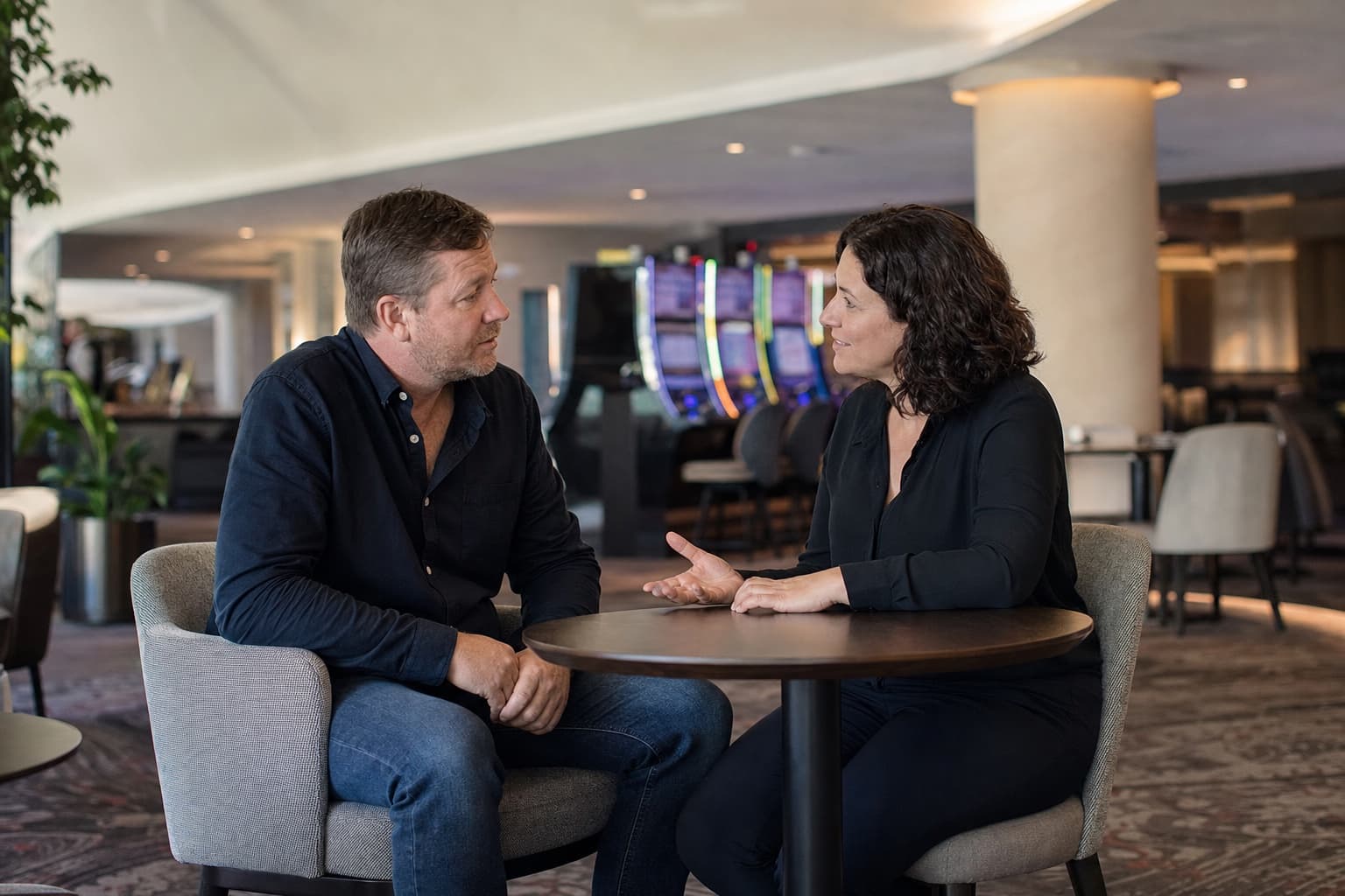 A senior venue worker has a calm responsible-gambling conversation with a patron away from the gaming floor